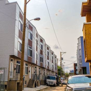 A row of apartment buildings with cars parked in front of them.