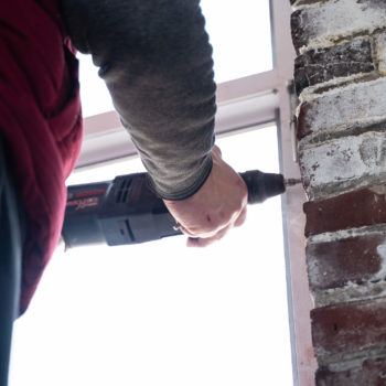 A man using a drill to fix a window.