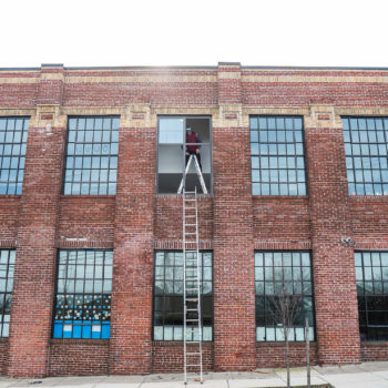 A man on a ladder on the side of a brick building.