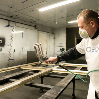 A man with a mask spraying a piece of wood.