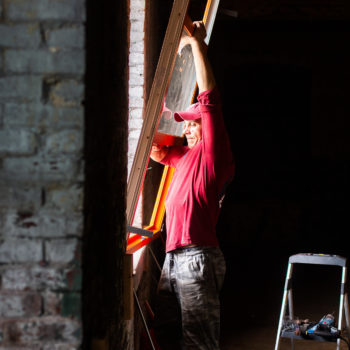 A man in a red shirt and jeans holding a window frame.