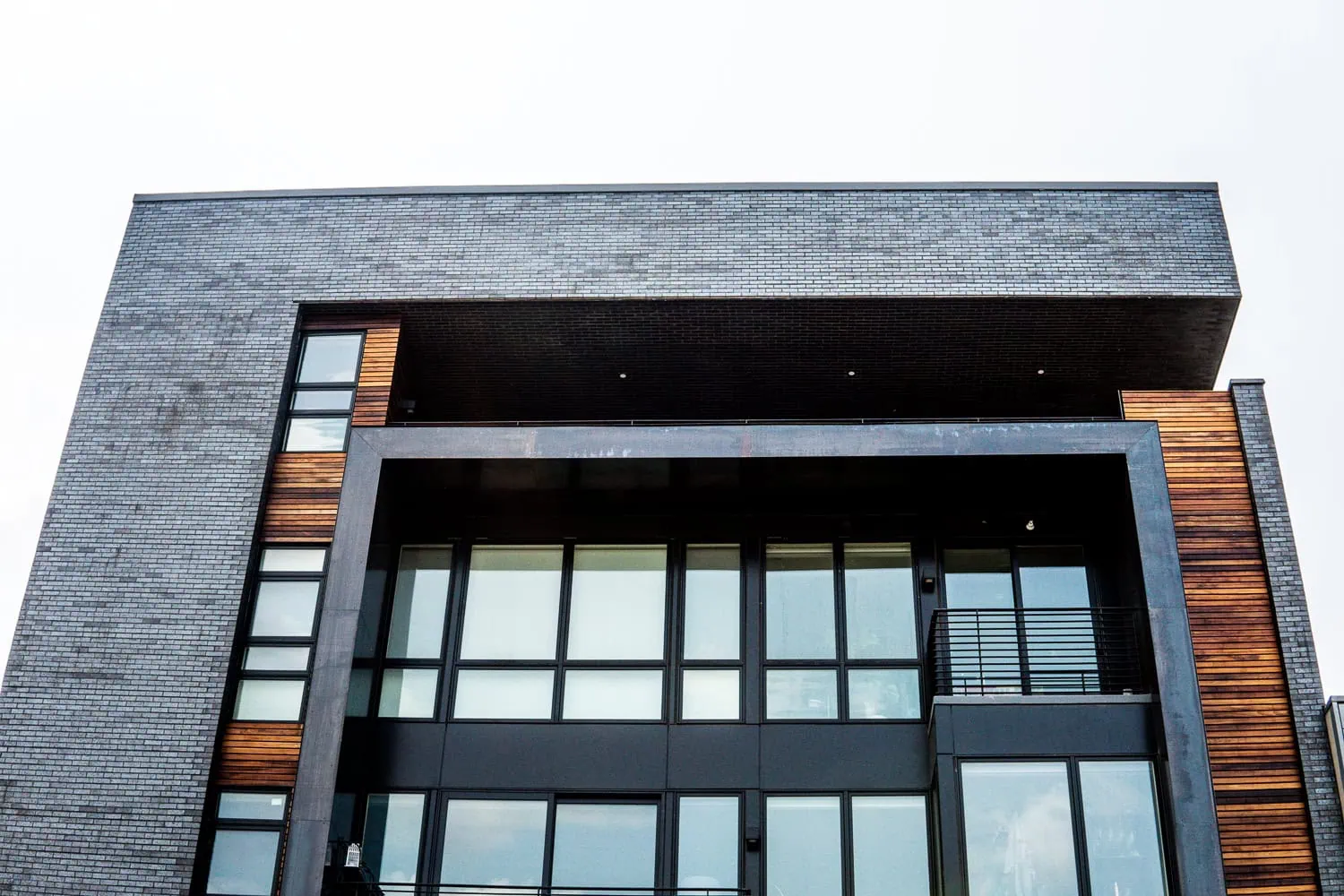 A modern multi-story building with a facade of dark bricks and large glass windows, accented by horizontal wooden panels and uPVC windows for time-tested durability.